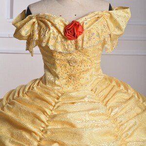May include: A yellow lace ball gown with a sweetheart neckline and a red rose accent. The gown has a fitted bodice and a full skirt.