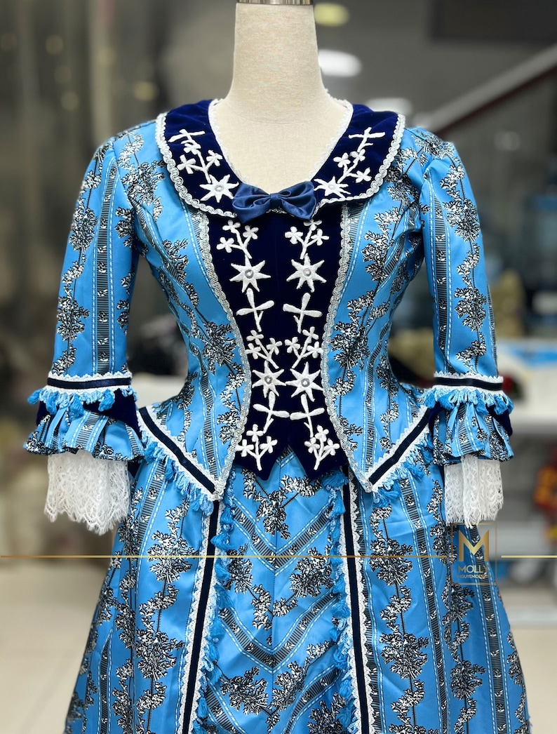 May include: A blue and white dress with a velvet collar and a floral pattern. The dress has a fitted bodice and a full skirt. The dress is decorated with white embroidery and black trim.