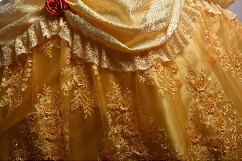 May include: A yellow satin and lace dress with a ruffled neckline and a floral pattern. The dress has a fitted bodice and a full skirt.
