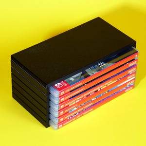 以下が含まれることがあります： 黒いプラスチック製のケースに、Nintendo Switchのゲームカートリッジが積み重ねられています。カートリッジは赤色で、白い文字が書かれています。ゲームタイトルは、Hollow Knight、ルイージマンション3、Nintendo World Championships NES Edition、スプラトゥーン3、スーパーマリオブラザーズワンダー、ワリオウェア！ゲットイットトゥギャザーです。