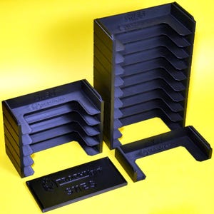 Puede incluir: Un conjunto de cajas de almacenamiento de pl&aacute;stico negro para cartuchos de juegos de video. Las cajas est&aacute;n apiladas en dos columnas, con la caja superior de cada columna etiquetada como "SNES" y "GAME BOY ADVANCE".