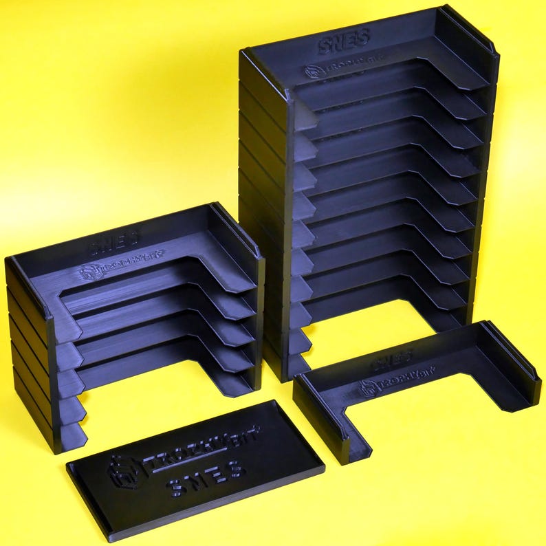 Puede incluir: Un conjunto de cajas de almacenamiento de pl&aacute;stico negro para cartuchos de juegos de video. Las cajas est&aacute;n apiladas en dos columnas, con la caja superior de cada columna etiquetada como "SNES" y "GAME BOY ADVANCE".