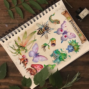 Puede incluir: Una página de cuaderno de bocetos con ilustraciones de acuarela de varios personajes de Pokémon, incluyendo una abeja, una mariposa, una rana y criaturas parecidas a plantas. La página está titulada "Pokémon" y tiene un borde en forma de rollo.