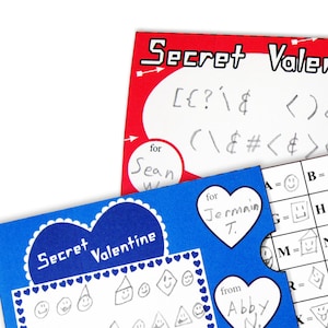 Puede incluir: Una tarjeta azul y blanca con forma de corazón que dice "Secret Valentine". La tarjeta tiene un código para descifrar un mensaje. El código es una cuadrícula con letras y símbolos.