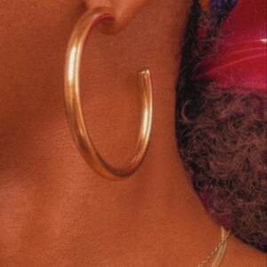 May include: A pair of large, gold hoop earrings. The earrings are thick and have a smooth, polished finish.
