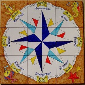 Peut inclure: Une tuile de céramique blanche avec une boussole comportant une étoile bleue au centre. La boussole est entourée d'une bordure de corde et porte les noms des directions du vent en italien écrits sur le bord. La tuile est décorée d'un poisson jaune, d'une étoile de mer rouge et d'un hippocampe jaune.