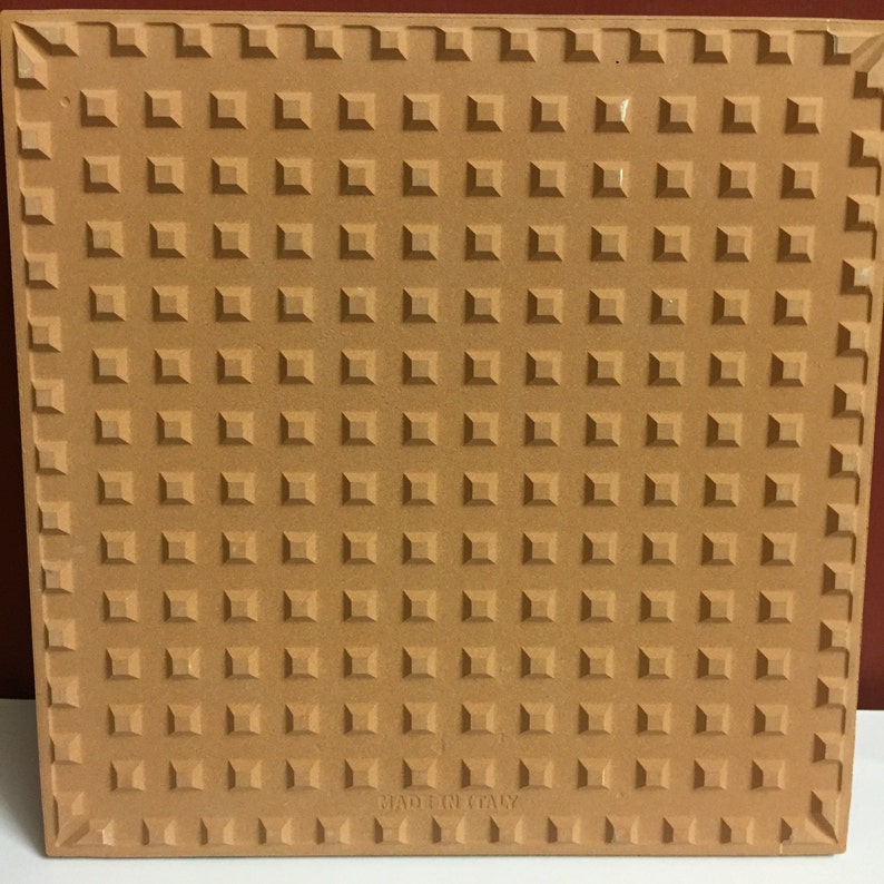 May include: A brown ceramic tile with a textured surface and the words "Made in Italy" printed on the bottom.