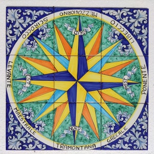 Peut inclure: Un carreau de céramique coloré en forme de boussole avec un motif d'étoile bleu, jaune et orange. Le carreau est entouré d'une bordure blanche avec les mots "LIBECCIO", "PONENTE", "GRECALE", "MAESTRALE", "LEVANTE", "SCIROCCO", "TRAMONTANA", "NORD", "MEZZOGIORNO", "SUD", "EST", "OVEST" écrits en italien.
