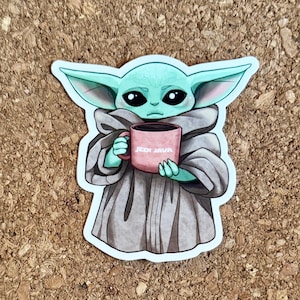 以下が含まれることがあります： 大きな耳と目を持つ漫画のキャラクターが、ピンク色のマグカップを持っているステッカー。マグカップには「JEDI JAVA」と書かれています。キャラクターは灰色のローブを着ており、薄緑色の肌をしています。