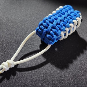 May include: A blue and white paracord keychain with a loop at the end. The keychain is made of braided cord and has a knot at the top.