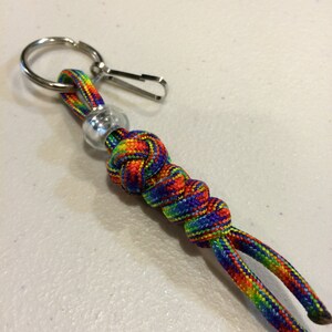 Op de afbeelding: Een regenboogkleurige paracord sleutelhanger met een zilveren metalen ring en een zilveren kraal.
