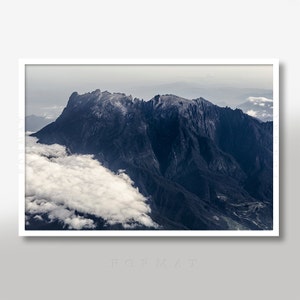 May include: An aerial view of a mountain range with a thick layer of clouds covering the lower slopes. The mountain peaks are visible above the clouds, with a dark blue hue.