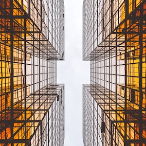 May include: Two tall buildings with a grid pattern of windows, viewed from below. The windows reflect the sky and create a geometric pattern.