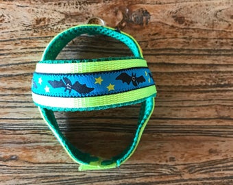 May include: Green and blue dog harness with a black bat and yellow star pattern.