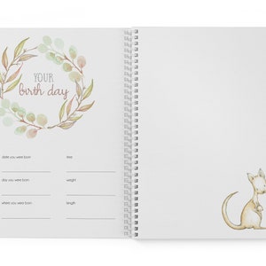 May include: A white spiral bound journal with a watercolor illustration of a wreath of leaves and the text "YOUR birth day". The journal has sections for recording the date, time, day, weight, and length of a baby's birth. The opposite page features a watercolor illustration of a kangaroo.