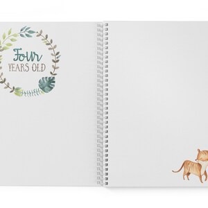 Puede incluir: Un cuaderno blanco de espiral con una corona de hojas verdes y marrones en la portada. La corona tiene el texto "Four Years Old" en su interior. La contraportada tiene una ilustraci&oacute;n de acuarela de un cachorro de tigre marr&oacute;n y naranja.