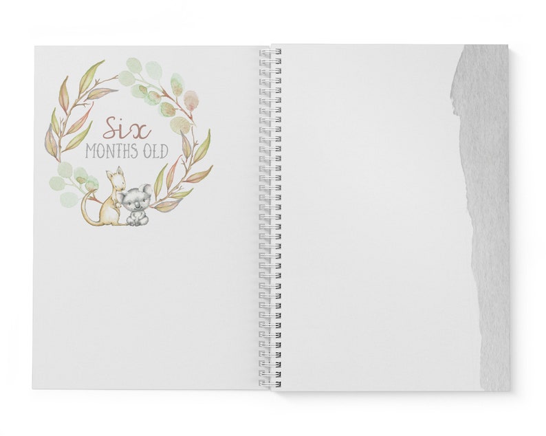May include: A white spiral bound journal with a watercolor illustration of a koala and a kangaroo in a wreath of green leaves. The text "Six Months Old" is written in brown lettering.