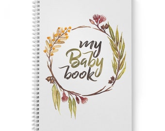 Può includere: Un diario bianco a spirale con una ghirlanda ad acquerello di foglie verdi, fiori gialli e fiori rosa. Il testo "my Baby book" è scritto in corsivo nero all'interno della ghirlanda.