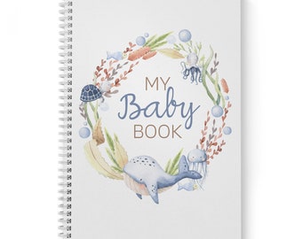 Può includere: Un libro per bambini rilegato a spirale blu e bianco con un'illustrazione ad acquerello di una balena, una tartaruga, un polpo e una medusa circondati da alghe e bolle. Il testo "My Baby Book" è scritto in lettere marroni.
