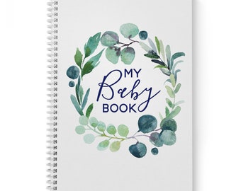 Può includere: Un quaderno bianco a spirale con una ghirlanda di foglie verdi e blu ad acquerello. Il testo "MY Baby BOOK" è scritto in corsivo blu scuro.