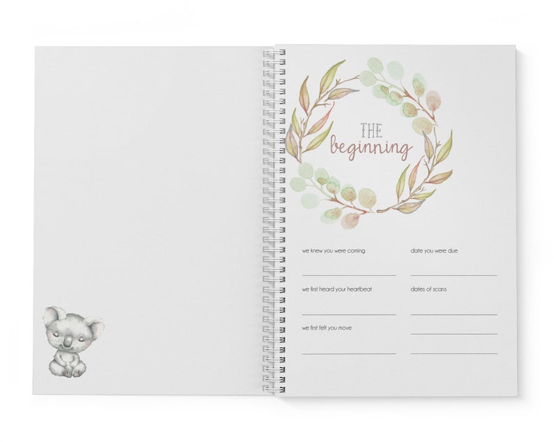 May include: A white journal with a watercolor wreath of leaves and the text "THE beginning" in pink. The journal has a spiral binding and a koala illustration on the left page.