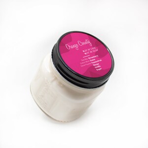 Puede incluir: Un tarro de vela rosa con una tapa negra. La etiqueta dice "Orange County" y enumera las coordenadas N.33 43 2.895 W.117 49 52.114. La vela est&aacute; perfumada con fresa, guayaba, maracuy&aacute;, mango, vainilla y az&uacute;car.