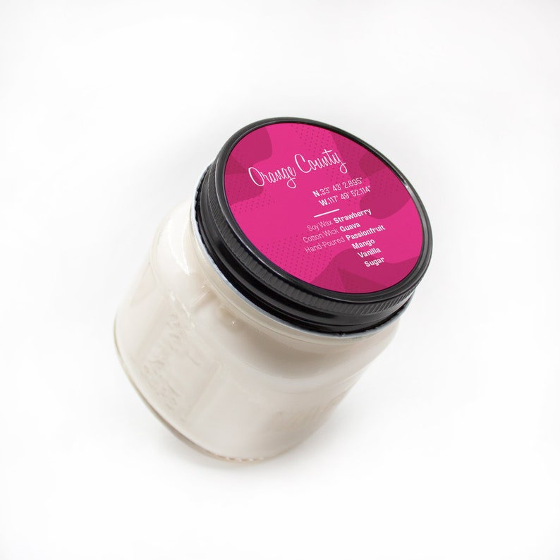 Puede incluir: Un tarro de vela rosa con una tapa negra. La etiqueta dice "Orange County" y enumera las coordenadas N.33 43 2.895 W.117 49 52.114. La vela est&aacute; perfumada con fresa, guayaba, maracuy&aacute;, mango, vainilla y az&uacute;car.