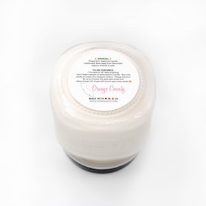 Puede incluir: Un tarro de vela blanco con una tapa negra y una etiqueta que dice "Orange County" con un contorno de California y un coraz&oacute;n. La etiqueta tambi&eacute;n incluye el texto "Made with Love in CA" y "www.nesnwaxco.com".