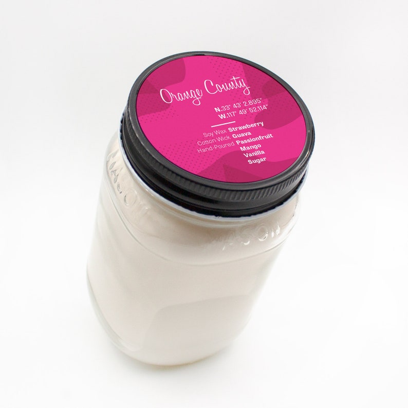 Puede incluir: Un tarro de vidrio transparente con una tapa negra. La tapa tiene una etiqueta rosa con el texto "Orange County" y coordenadas. La etiqueta tambi&eacute;n enumera el aroma de la vela: Fresa, Guayaba, Maracuy&aacute;, Mango, Vainilla, Az&uacute;car. Cera de soja, Mecha de algod&oacute;n, Hecho a mano.