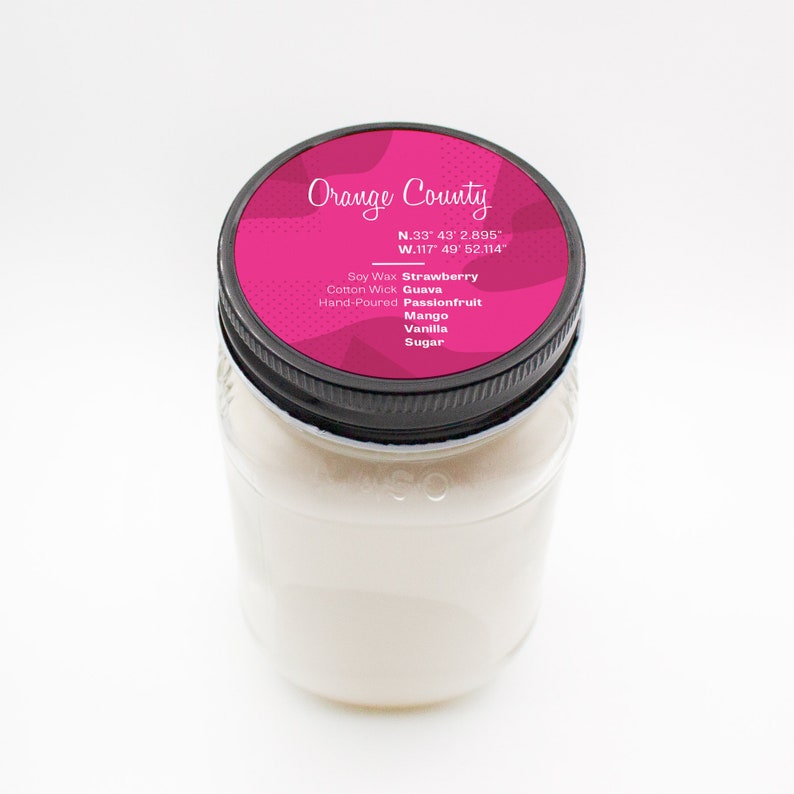 Puede incluir: Una vela de vidrio en un frasco con una tapa negra. La tapa tiene una etiqueta rosa con el texto "Orange County" y coordenadas. La etiqueta tambi&eacute;n enumera las fragancias: Fresa, Guayaba, Maracuy&aacute;, Mango, Vainilla y Az&uacute;car. La vela est&aacute; hecha a mano y hecha con cera de soya y una mecha de algod&oacute;n.