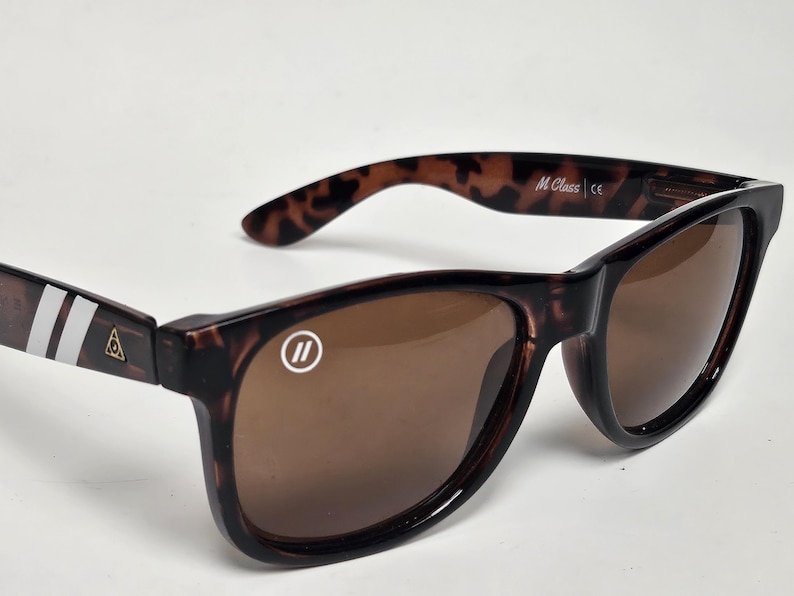 May include: Tortoiseshell sunglasses with brown lenses. The left lens features a white circular logo with two vertical lines. The temples display two white stripes and a small gold triangular emblem. The inner temple is printed with M Class.