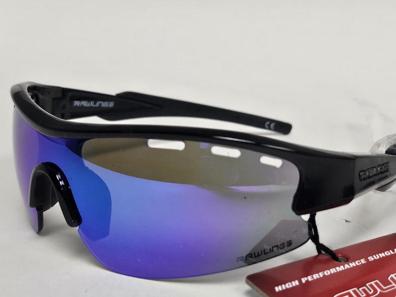 K&ouml;nnte beinhalten: Schwarze Rawlings-Sonnenbrille mit blau verspiegelten Gl&auml;sern. Die Sonnenbrille hat ein sportliches Design mit einem umlaufenden Rahmen. Das Rawlings-Logo ist auf dem Rahmen und den Gl&auml;sern sichtbar. Ein Etikett mit "HIGH PERFORMANCE SUNGL" ist angebracht.