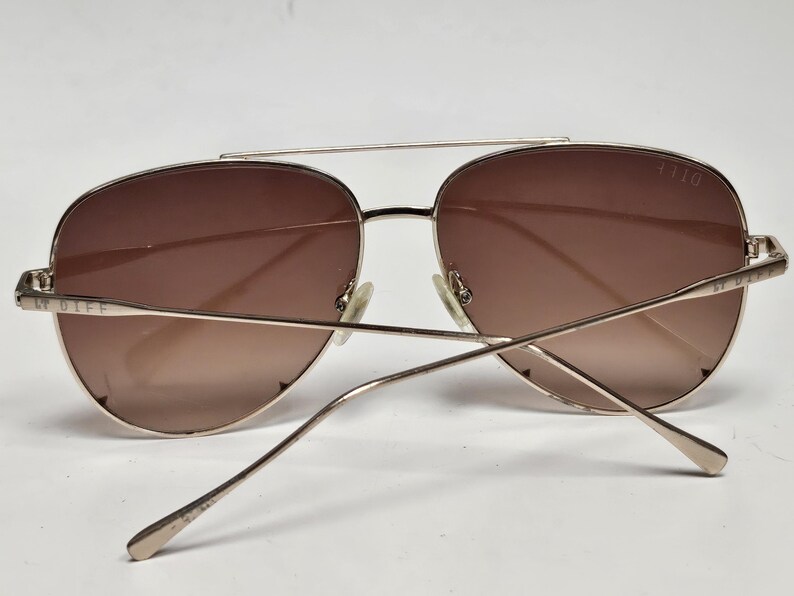 Puede incluir: Gafas de sol estilo aviador con montura de metal dorado y lentes degradadas marrones. Las finas patillas se extienden hacia atr&aacute;s, con "DIFF" visible en la patilla izquierda. El n&uacute;mero "1110" est&aacute; en la barra superior.