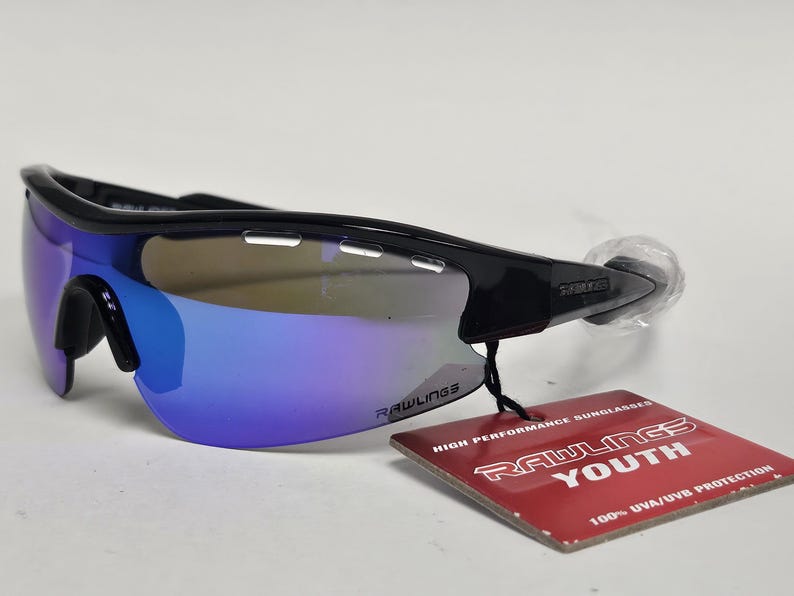 K&ouml;nnte beinhalten: Schwarze Rawlings-Sonnenbrille f&uuml;r Jugendliche mit blau verspiegelten Gl&auml;sern. Die Sonnenbrille hat ein sportliches Design und ein Etikett mit der Aufschrift "Rawlings Youth" und "100% UVA/UVB Protection."
