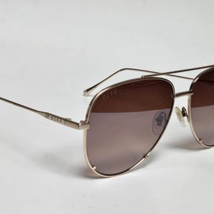 Puede incluir: Gafas de sol aviador en oro rosa con lentes degradadas marrones. Las gafas tienen un doble puente y varillas finas. La marca "DIFF" es visible en la varilla. Las lentes son de color marr&oacute;n claro.