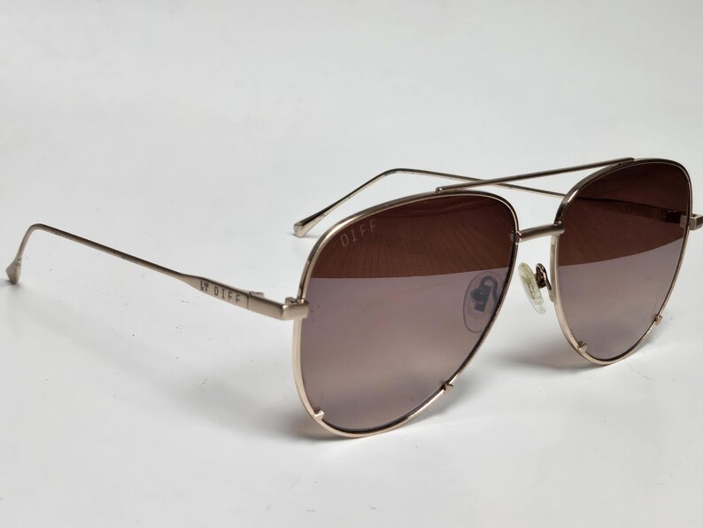 Puede incluir: Gafas de sol aviador en oro rosa con lentes degradadas marrones. Las gafas tienen un doble puente y varillas finas. La marca "DIFF" es visible en la varilla. Las lentes son de color marr&oacute;n claro.