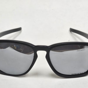 May include: Black sunglasses with green accents and mirrored lenses. The lenses have the word "PRIZM" printed on them.