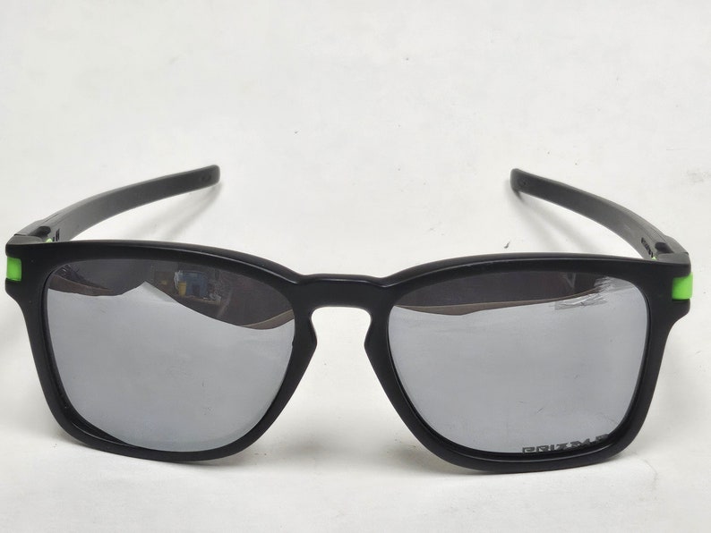 May include: Black sunglasses with green accents and mirrored lenses. The lenses have the word "PRIZM" printed on them.