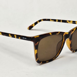 Peut inclure: Lunettes de soleil en écaille de tortue avec des verres bruns. Les lunettes ont une monture carrée.