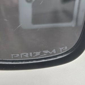 May include: Close-up of a black framed mirror with the text "PRIZM P" printed on the glass.
