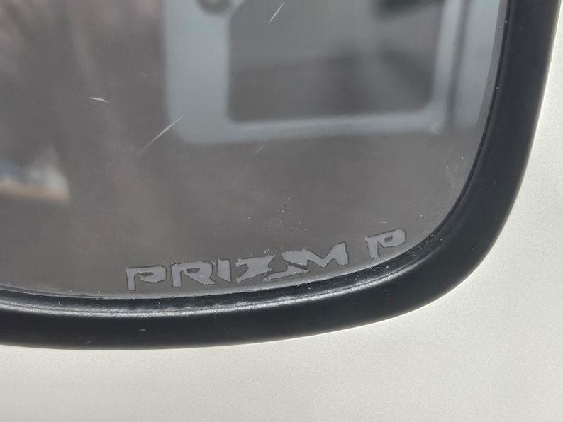 May include: Close-up of a black framed mirror with the text "PRIZM P" printed on the glass.
