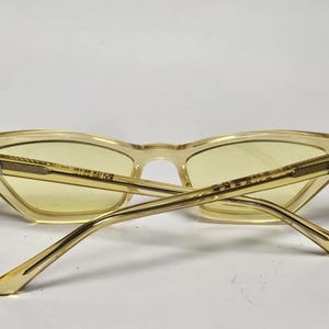 K&ouml;nnte beinhalten: Katzenaugen-Sonnenbrille mit einem durchscheinenden blassgelben Rahmen und passenden hellgelb get&ouml;nten Gl&auml;sern. Die B&uuml;gel verf&uuml;gen &uuml;ber eine strukturierte goldfarbene Metalleinlage mit einem kleinen silberfarbenen Akzent am Scharnier.