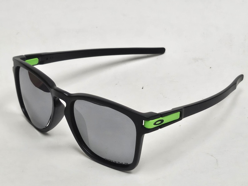 May include: Black sunglasses with green accents. The lenses are dark gray and the frame is made of plastic.