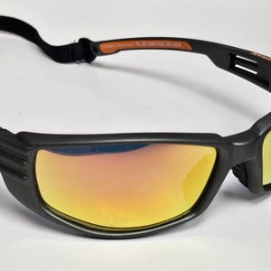 May include: Black sports sunglasses with orange and yellow mirrored lenses. The sunglasses have a black strap and the brand name "Body Glove" is visible on the side. The lenses are rectangular and the frame is thick.