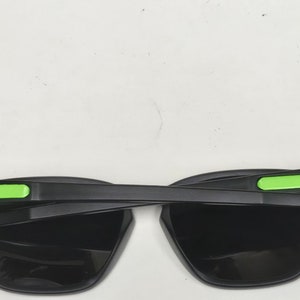 May include: Black sunglasses with green accents on the arms. The lenses are black and the frame is made of plastic.