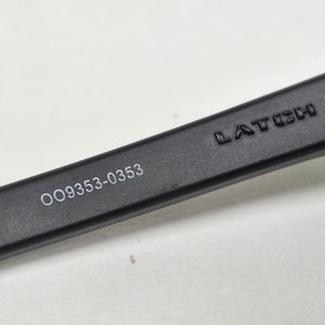 May include: Close-up of a black sunglasses arm with the text "LATCH" and "OO9353-0353" printed on it.
