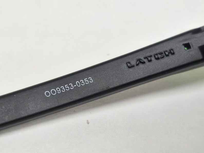 May include: Close-up of a black sunglasses arm with the text "LATCH" and "OO9353-0353" printed on it.