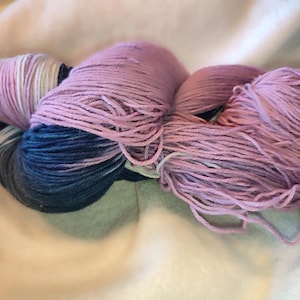 Könnte beinhalten: Ein Knäuel Garn in den Farbtönen Lavendel, Rosa, Weiß und Marineblau. Das Garn ist locker gewickelt, mit sichtbaren Strähnen. Das Garn ist wahrscheinlich für Strick- oder Häkelprojekte.