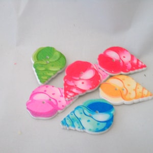 Könnte beinhalten: Sechs bunte, muschelförmige Knöpfe auf weißem Hintergrund. Die Knöpfe sind in den Farben Rosa, Grün, Blau, Gelb und Rot bemalt.