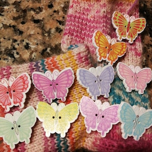 Könnte beinhalten: Nahaufnahme einer gestrickten Socke mit verschiedenen bunten Schmetterlingsknöpfen. Die Knöpfe sind aus Holz und haben eine lackierte Oberfläche.